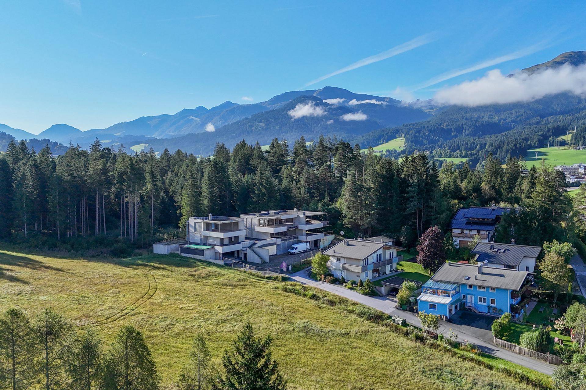 Luftaufnahme eines modernen Gebäudekomplexes in ländlicher Umgebung mit Wald und Bergen.