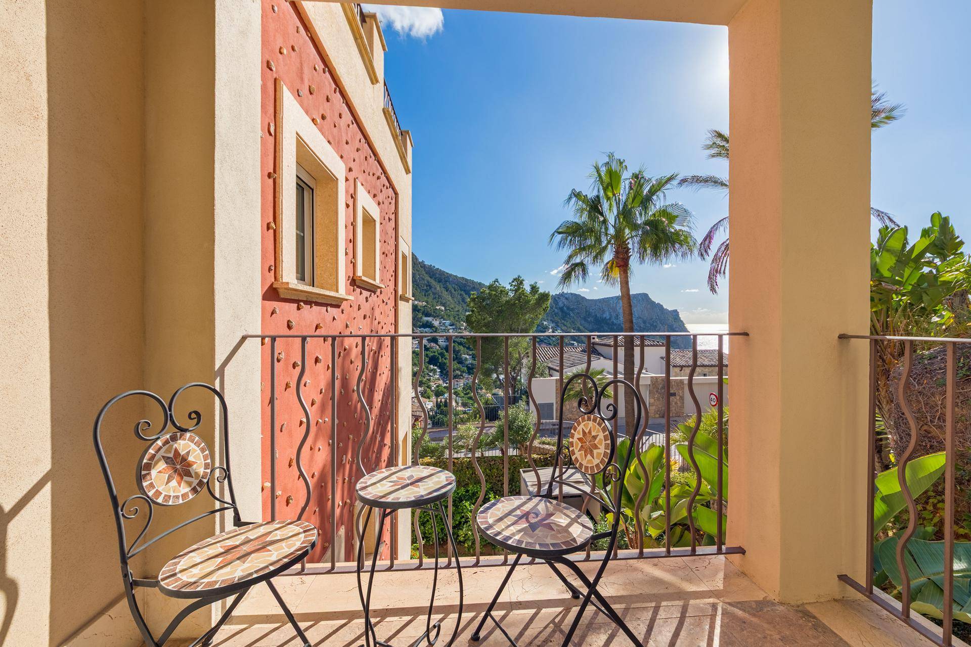 Kleiner Balkon mit schmiedeeisernen Stühlen und Tisch, bietet Blick auf Palmen und Berge.