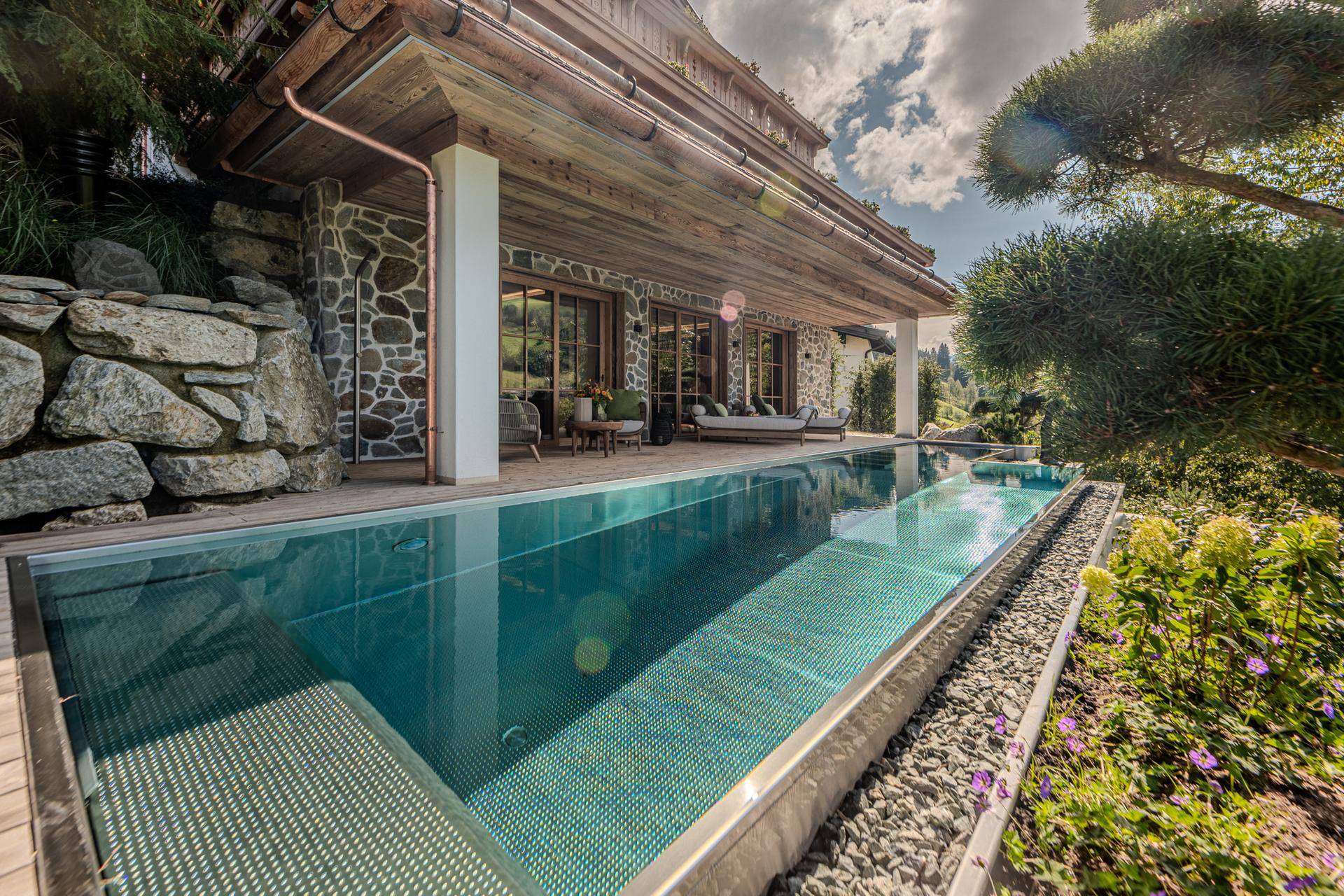 Langer Infinity-Pool entlang der Holzterrasse mit Blick auf die umliegende Berglandschaft.
