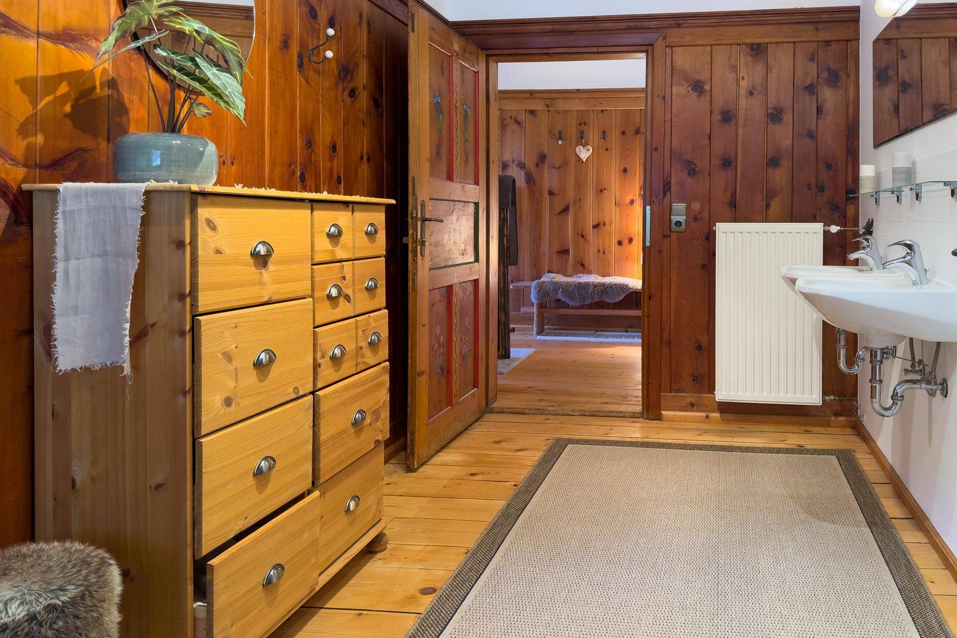 Badezimmerbereich mit Holzkommode, Waschbecken und Holzboden, der zu einem weiteren Raum führt.
