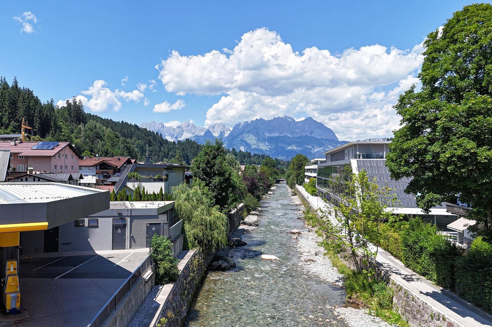 Flusslauf durch die Stadt mit Brücken und einer beeindruckenden Bergkulisse im Hintergrund.