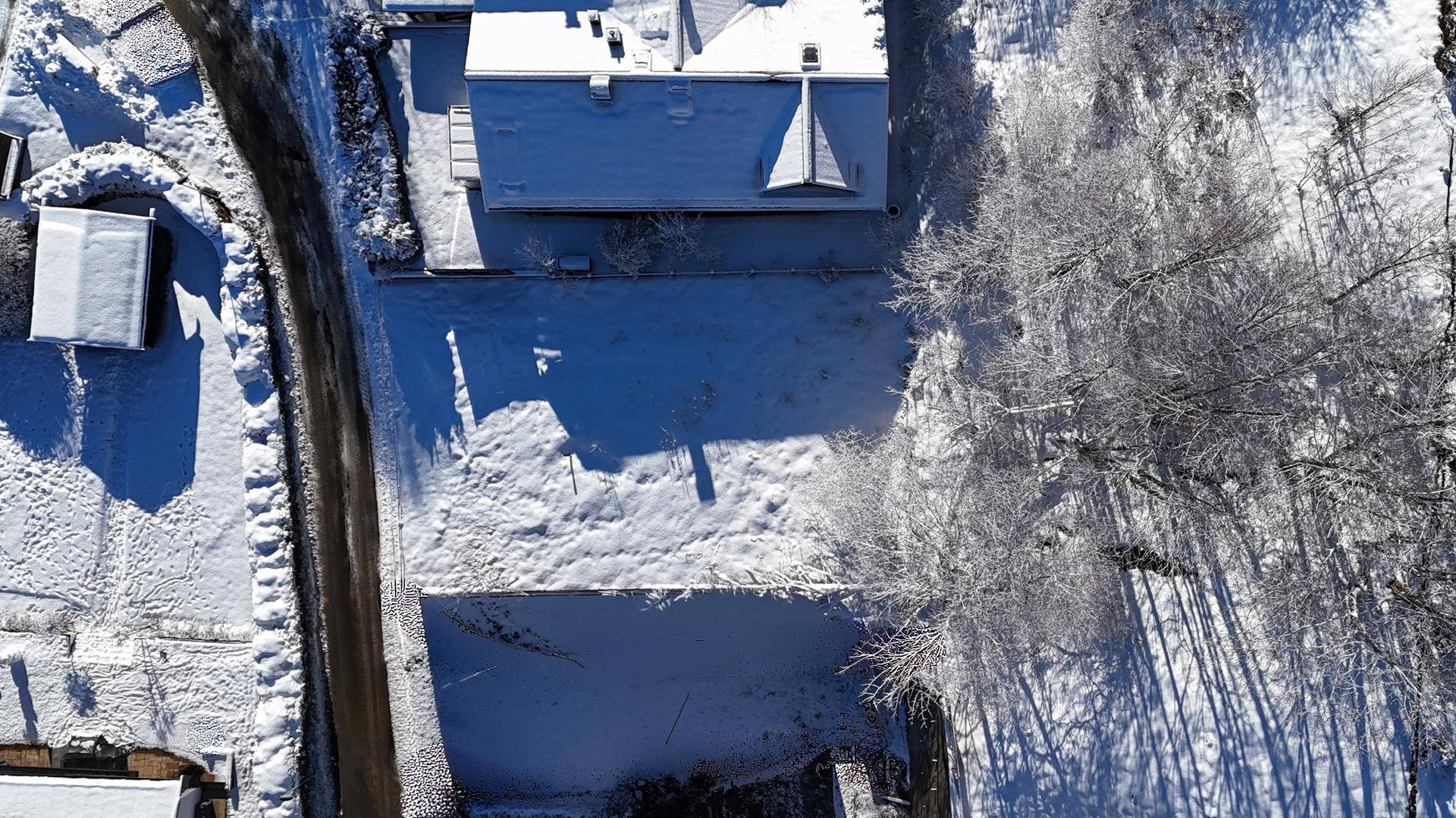 Luftaufnahme eines schneebedeckten Grundstücks mit einem Haus und umliegenden Bäumen.