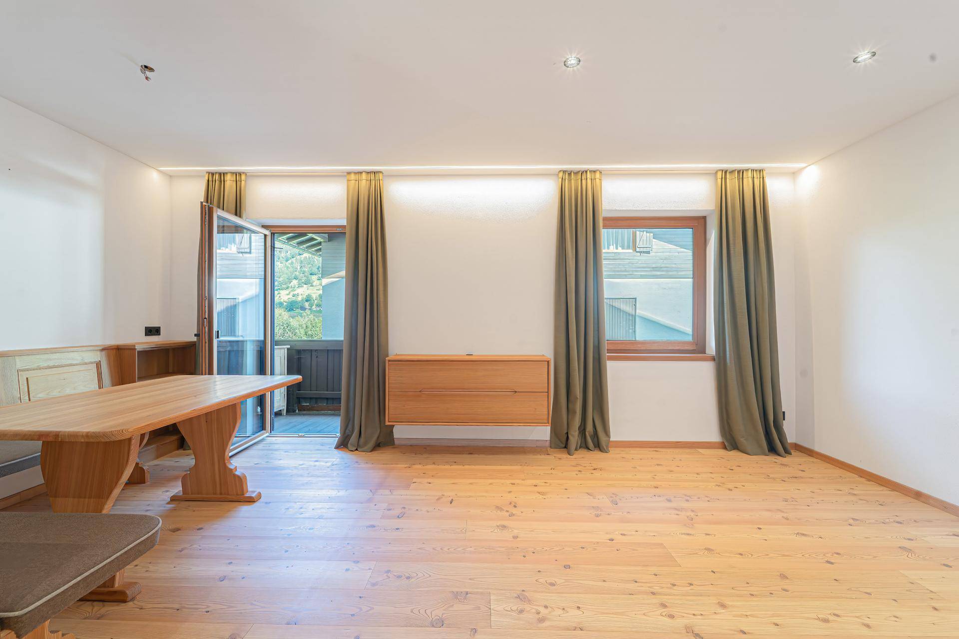 Lichtdurchfluteter Wohnbereich mit Holzboden, Zugang zum Balkon und Blick ins Grüne.