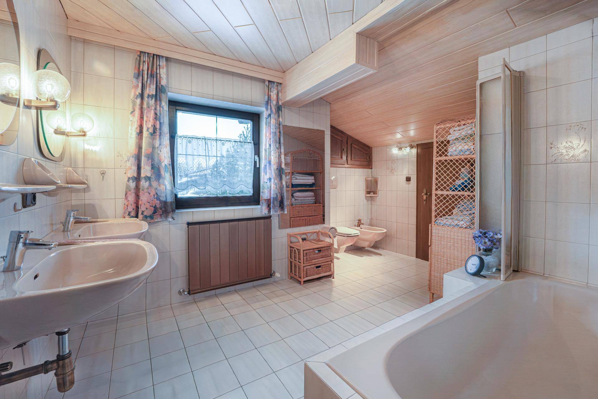 Helles Badezimmer mit Doppelwaschbecken, Badewanne und Holzverkleidung an der Decke.