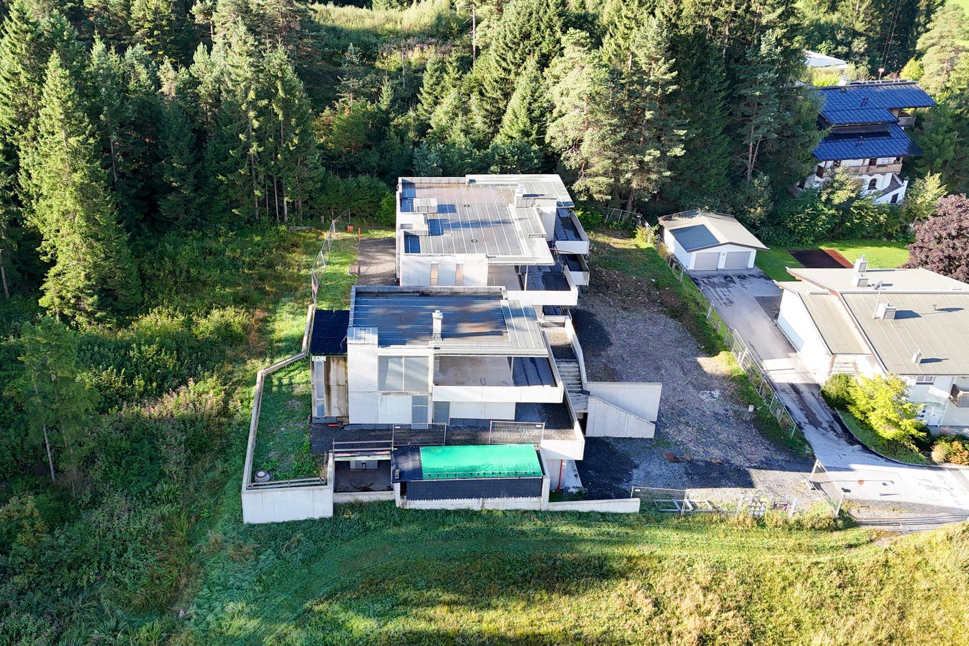 Draufsicht auf den modernen Gebäudekomplex mit Flachdächern und angrenzendem Waldgebiet.