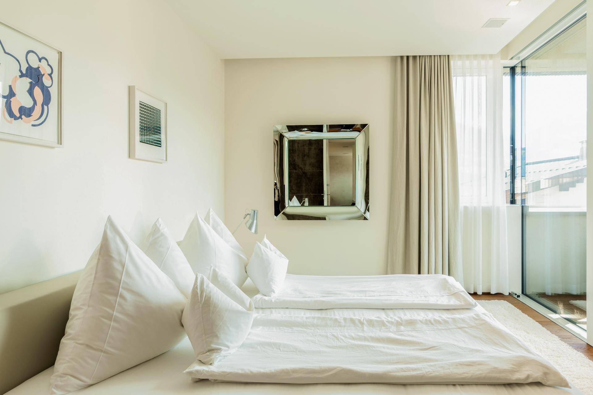 Helles Schlafzimmer mit Doppelbett, weißer Bettwäsche und Zugang zu einem Balkon.