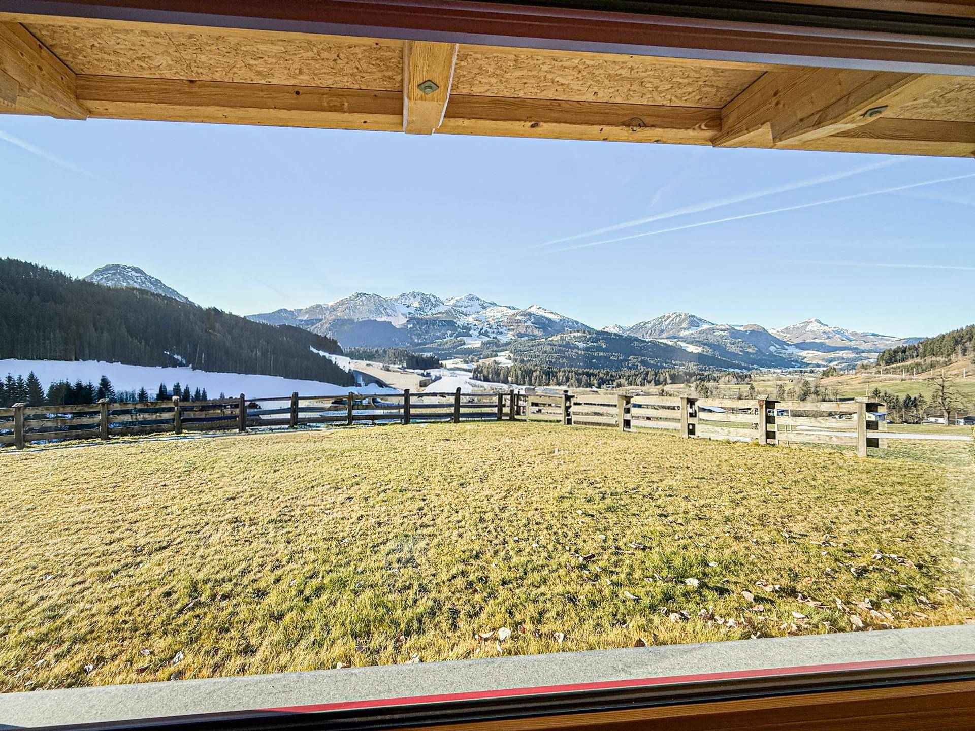 Panoramablick auf die schneebedeckten Berge und grüne Felder von einem Balkon oder Fenster.