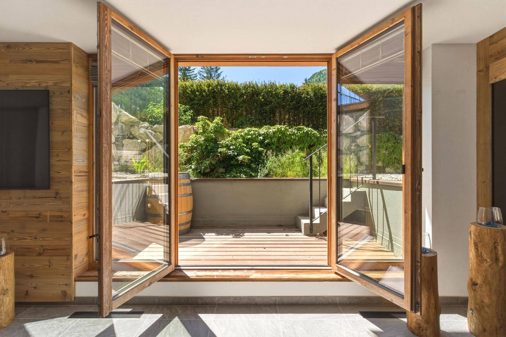 Heller Innenraum mit großen Glastüren, die sich zu einer privaten Terrasse mit Hecke öffnen.