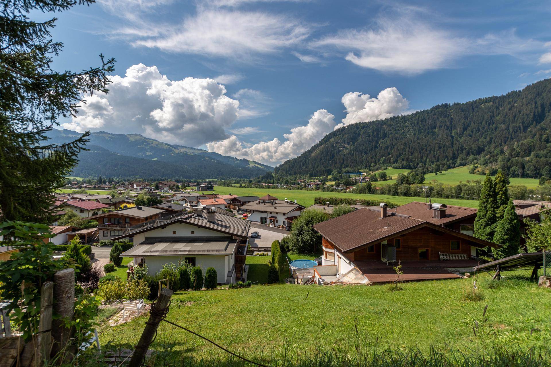 Panoramablick auf ein malerisches Dorf in den Bergen, umgeben von grünen Wiesen und Wäldern.