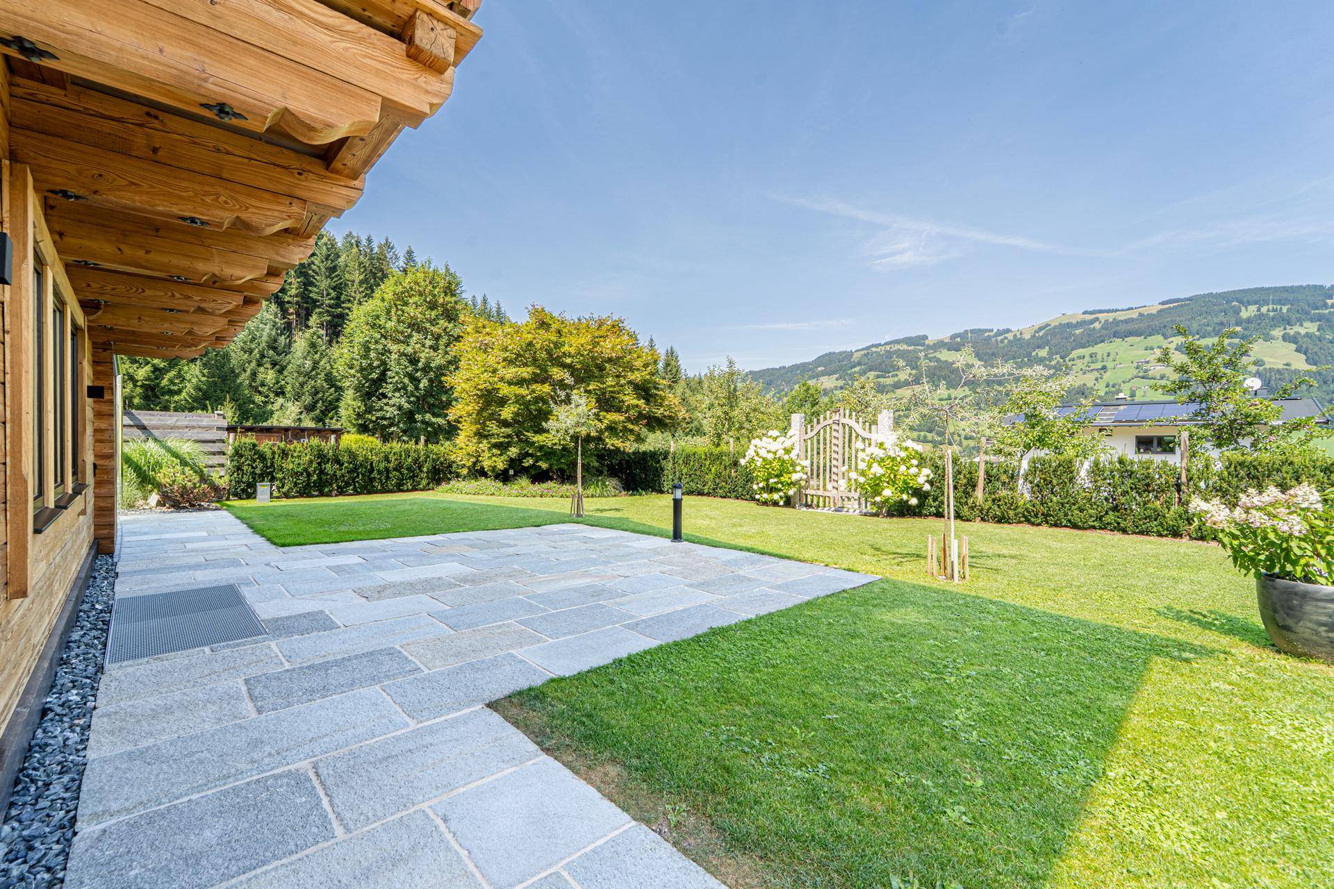Sonniger Terrassenbereich mit Steinplatten und weitläufigem Blick auf die grüne Hügellandschaft.
