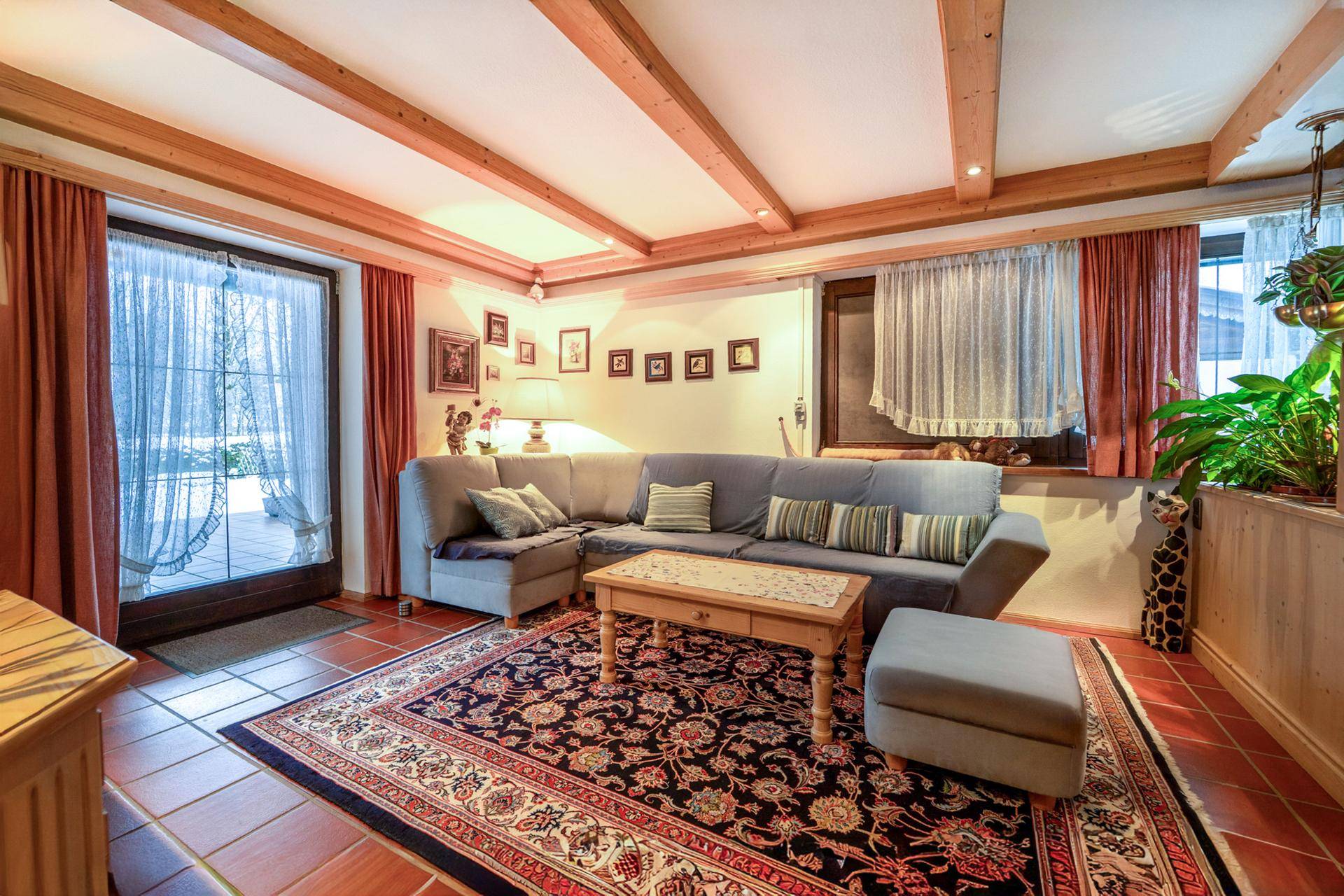 Gemütliches Wohnzimmer mit Holzbalkendecke, Terrakottafliesen und Zugang zur Terrasse.