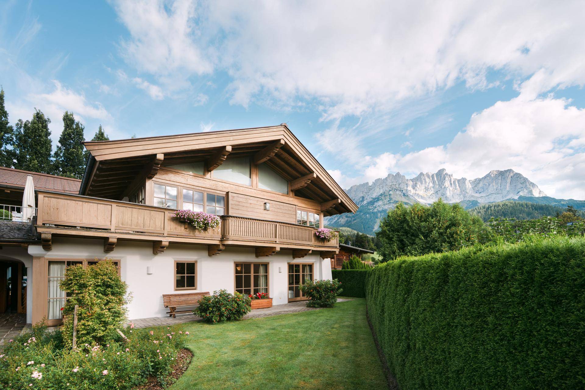 Charmantes Landhaus mit traditioneller Holzfassade und gepflegtem Garten vor beeindruckender Bergkulisse.