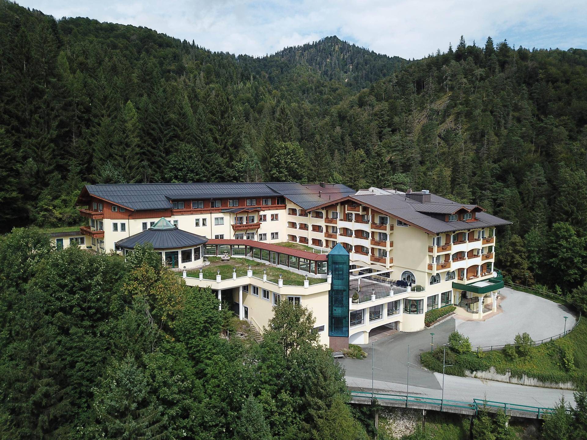 Detailreiche Luftaufnahme eines Hotels im alpinen Stil, eingebettet in eine bewaldete Berglandschaft.