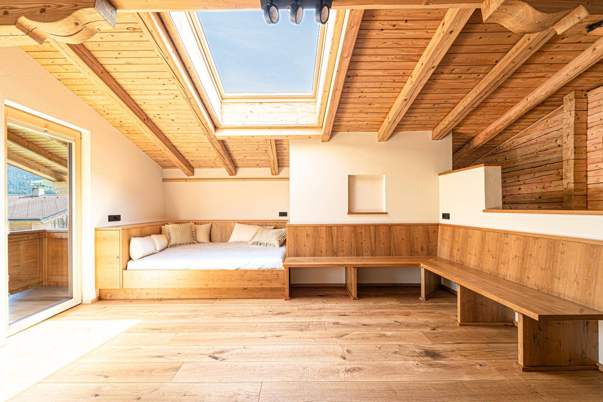 Gemütliches Schlafzimmer im Dachgeschoss mit Holzbalkendecke, Dachfenster und integrierten Holzmöbeln.