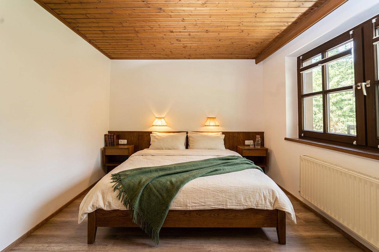 Schlafzimmer mit Holzbett, Holzdecke und Fenster mit Blick ins Grüne.
