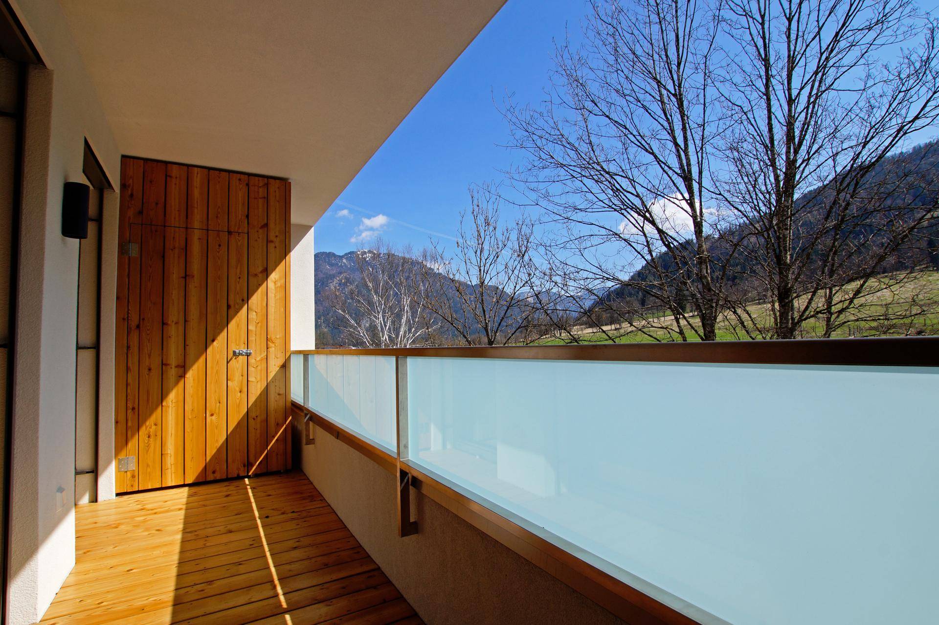 Sonniger Balkon mit Holzboden, Glasbrüstung und herrlichem Blick auf die umliegenden Berge.