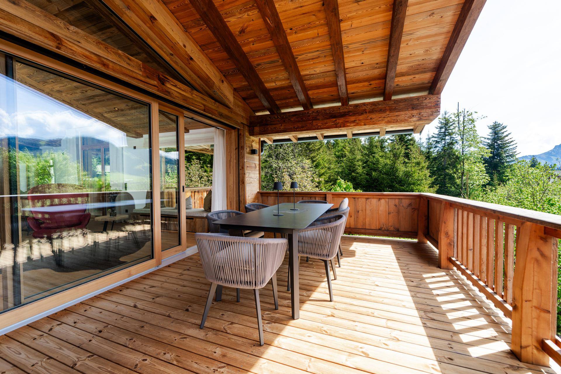 Geräumiger Holzbalkon mit Esstisch und Stühlen, ideal für Mahlzeiten im Freien mit Waldblick.