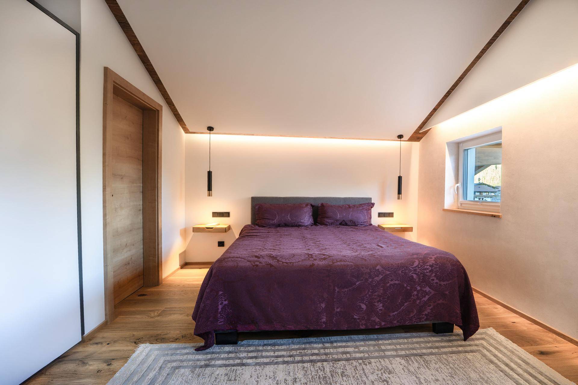 Ruhiges Schlafzimmer mit Doppelbett, Holzbalken und indirekter Beleuchtung.