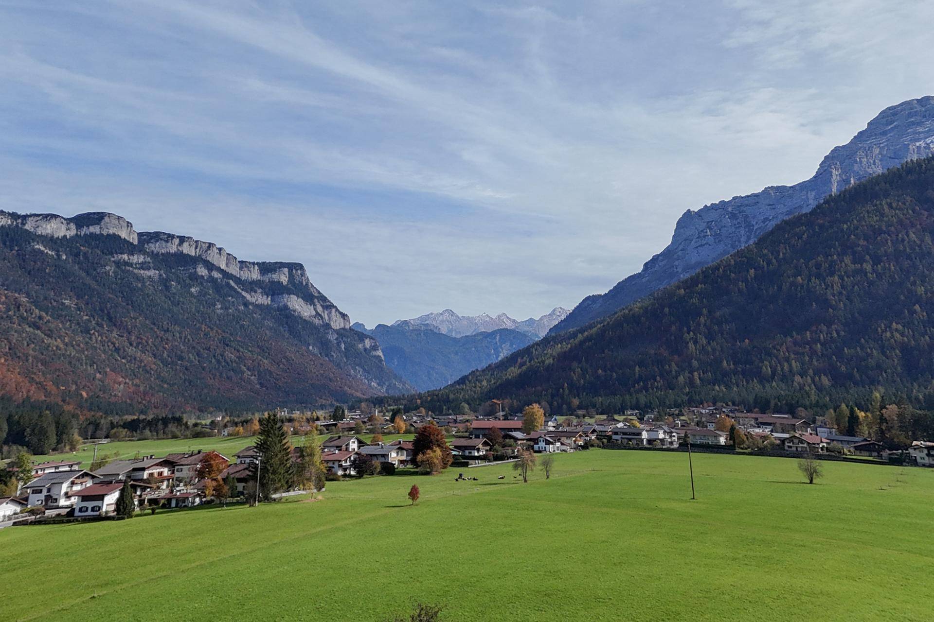 Weitläufige Landschaft mit Bergen, grünen Wiesen und einem Dorf im Tal.