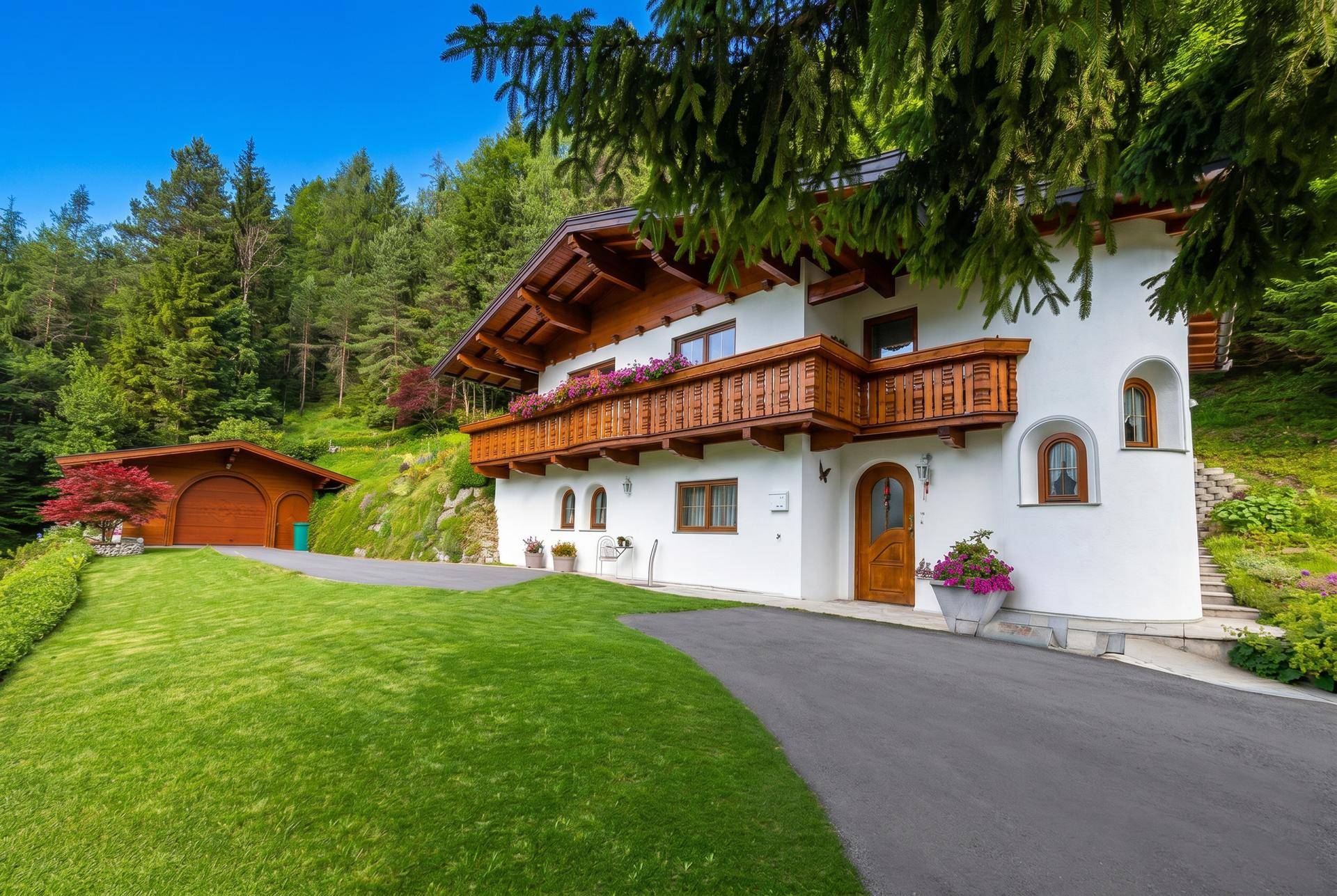 Charmantes Landhaus mit Holzbalkonen und gepflegter Auffahrt vor bewaldeter Bergkulisse.
