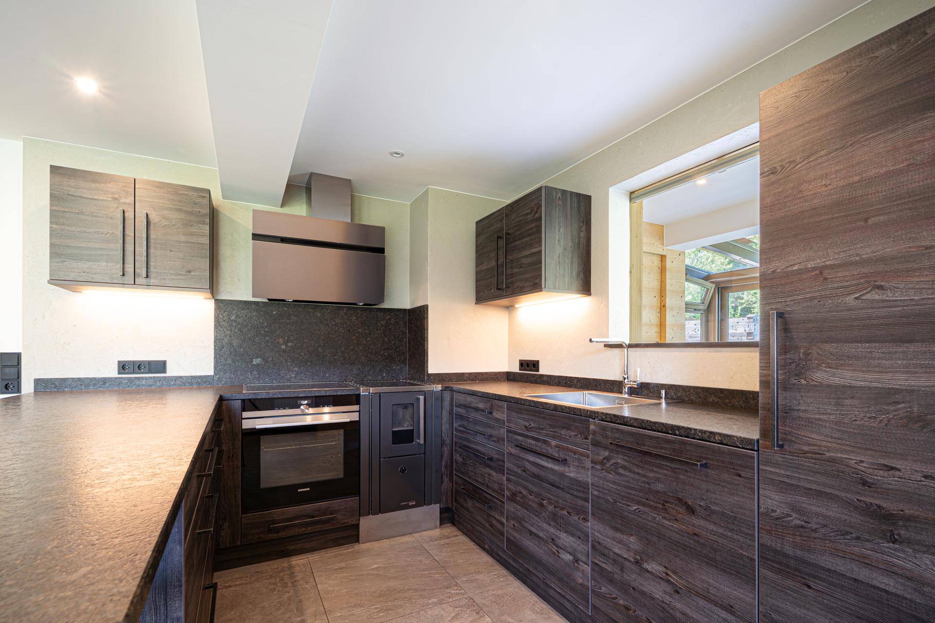 Moderne Einbauküche mit dunklen Holzschränken, Stein-Arbeitsplatte und integrierten Siemens-Geräten.