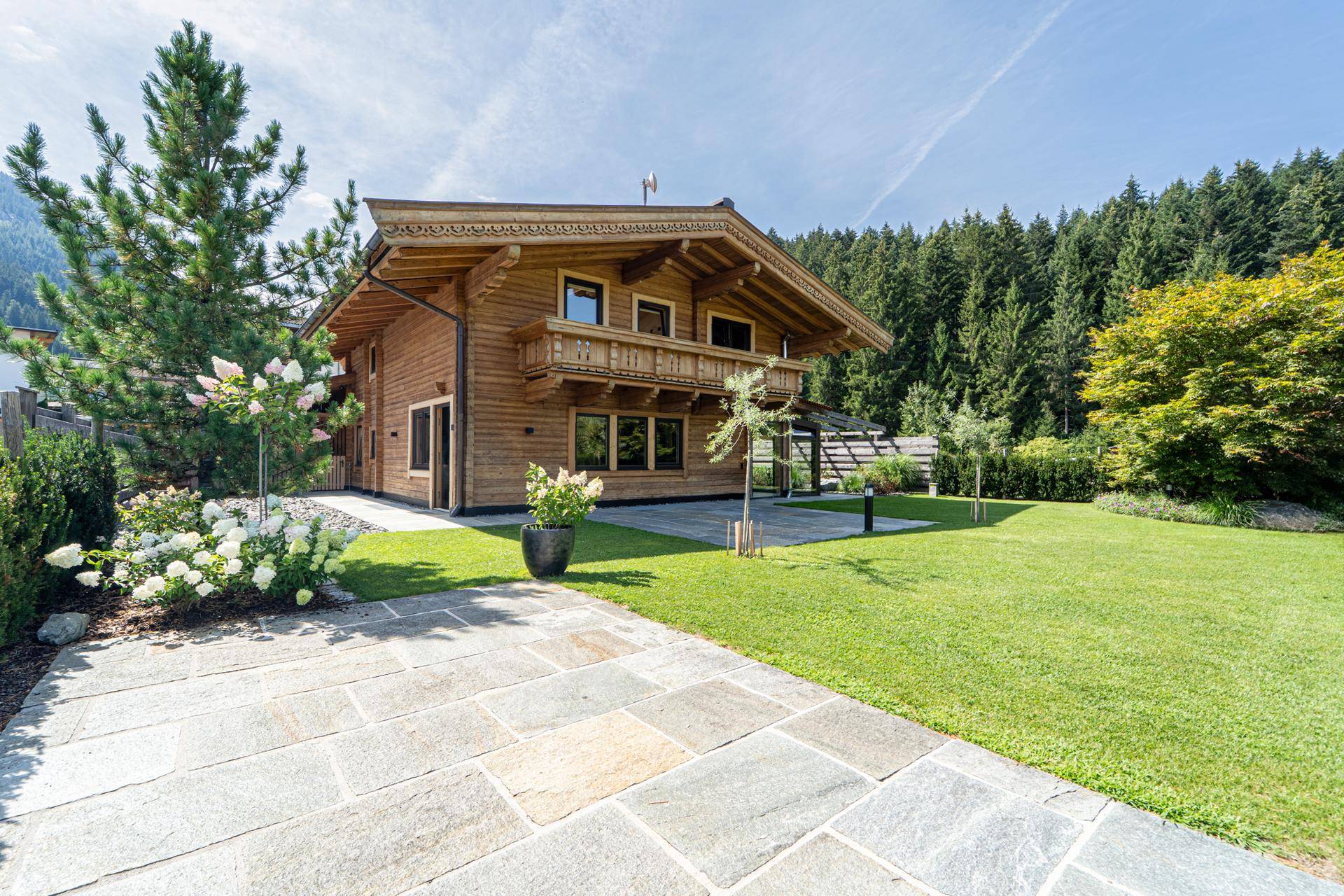Idyllischer Gartenbereich mit Rasenfläche, Steinplattenweg und traditionellem Holzhaus im Hintergrund.