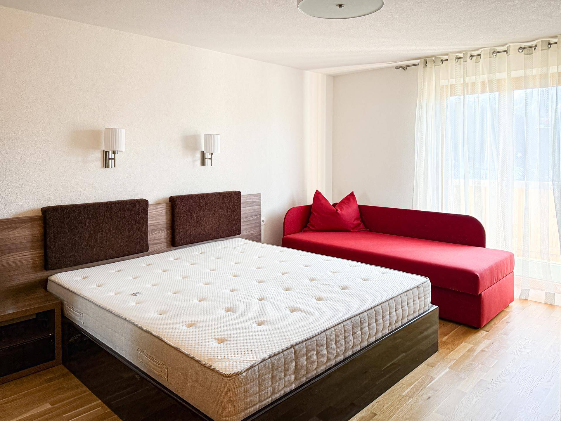 Gemütliches Schlafzimmer mit Holzboden, rotem Sofa und großem Doppelbett.