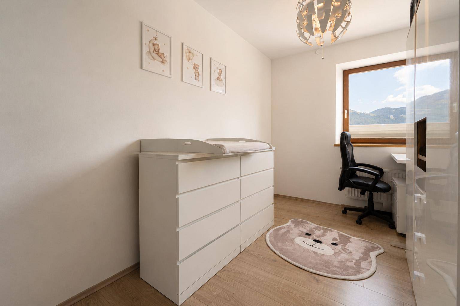 Kinderzimmer mit Wickelkommode, Schreibtisch und Blick auf die umliegende Landschaft.
