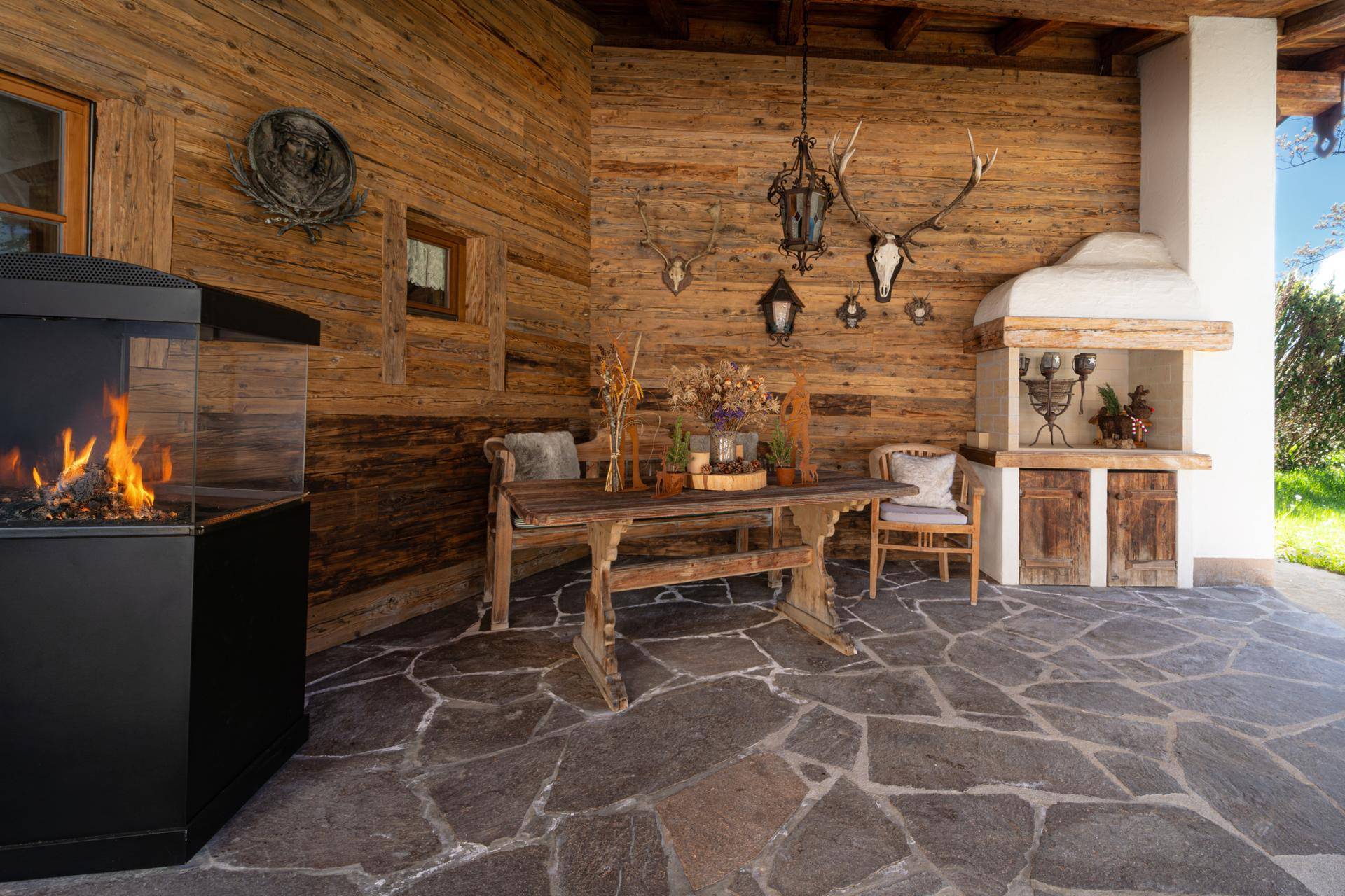 Überdachte Terrasse im alpinen Stil mit Steinfliesen, Holzwänden, Kamin und traditioneller Dekoration.