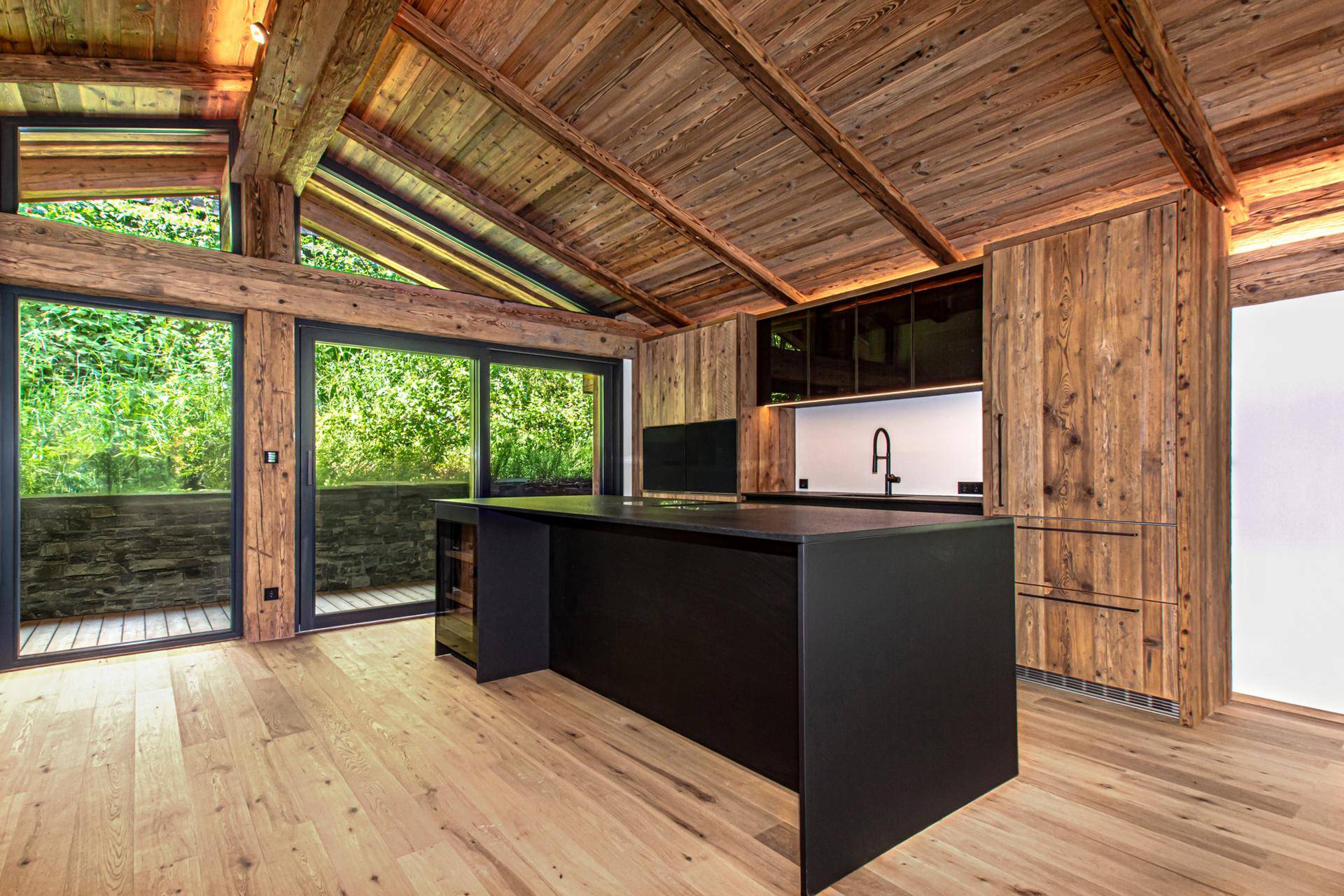 Offene Küche mit schwarzer Kücheninsel, Holzbalkendecke und Zugang zu einem Balkon mit Bergblick.