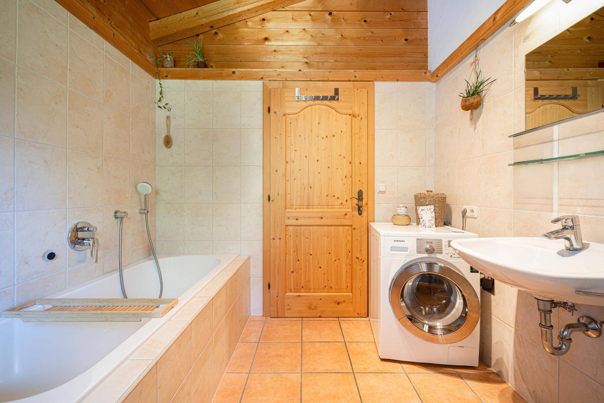 Helles Badezimmer mit Badewanne, Waschbecken und Waschmaschine, ausgestattet mit Terrakotta-Fliesen.
