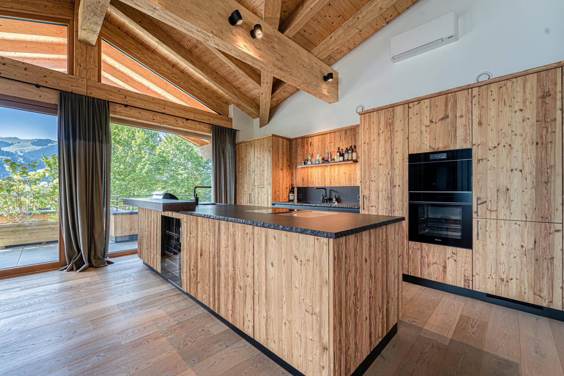 Moderne Holzküche mit großer Kochinsel, integrierten Geräten und Panoramablick auf die Berge.