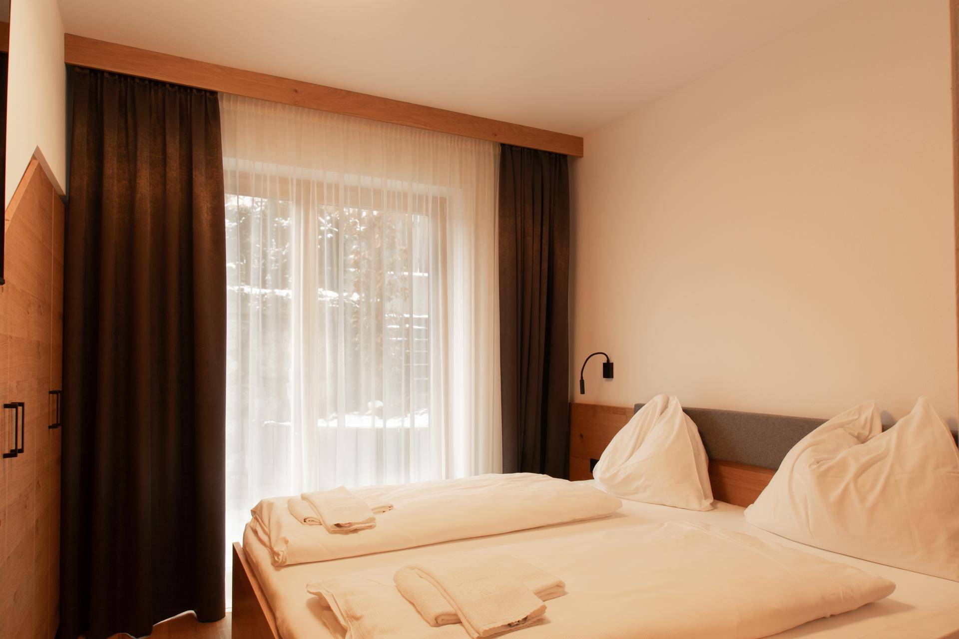 Komfortables Schlafzimmer mit Holzboden und großen Fenstern, die viel Licht hereinlassen.