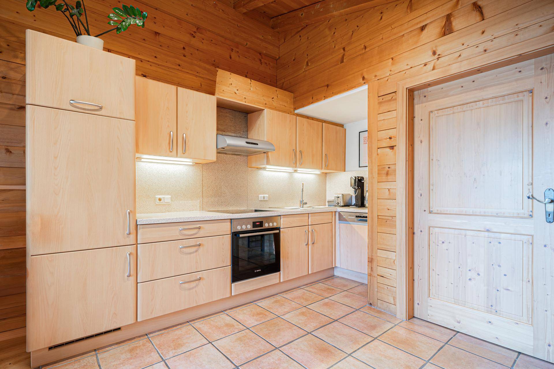 Funktionale Holzküche mit hellen Schränken, integrierten Geräten und Terrakotta-Fliesenboden.