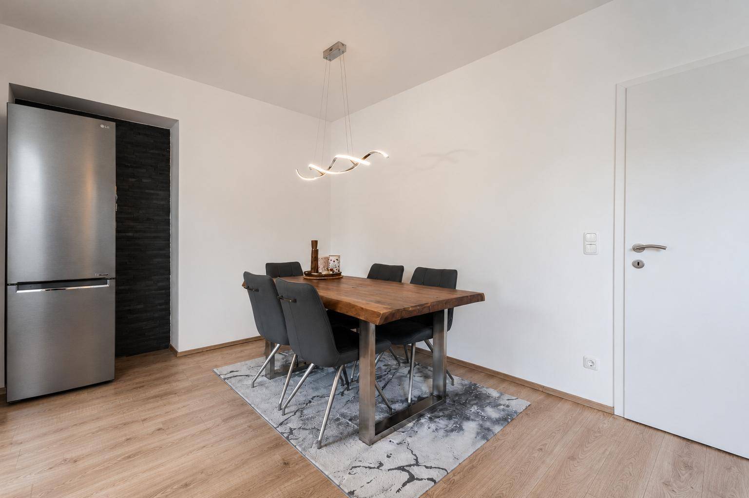 Essbereich mit rustikalem Holztisch, modernen Stühlen und großem Kühlschrank.