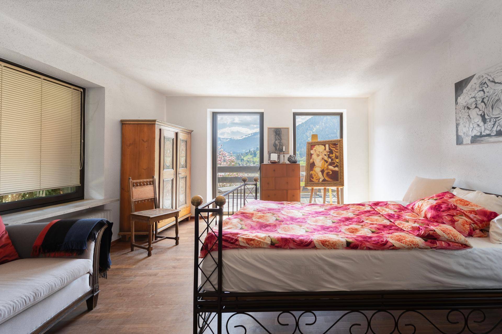 Schlafzimmer mit schmiedeeisernem Bett, Holzboden und Fenstern mit Bergblick.