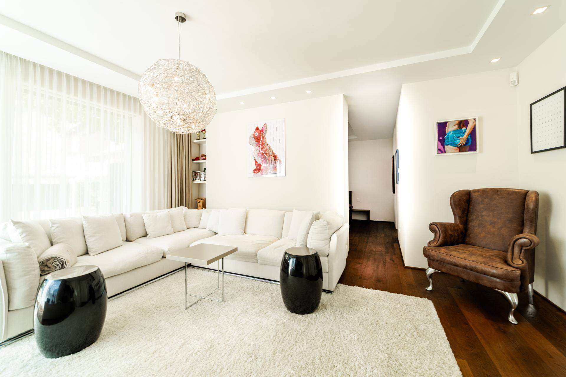 Modernes Wohnzimmer mit weißem Ecksofa, dunklem Holzboden und auffälliger Deckenleuchte.