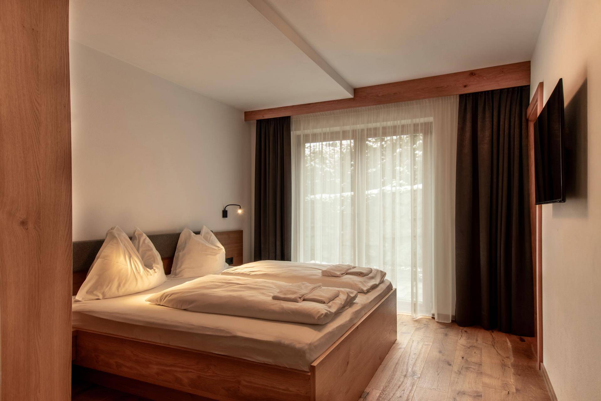 Helles Schlafzimmer mit Doppelbett, Holzboden und Zugang zum Balkon.