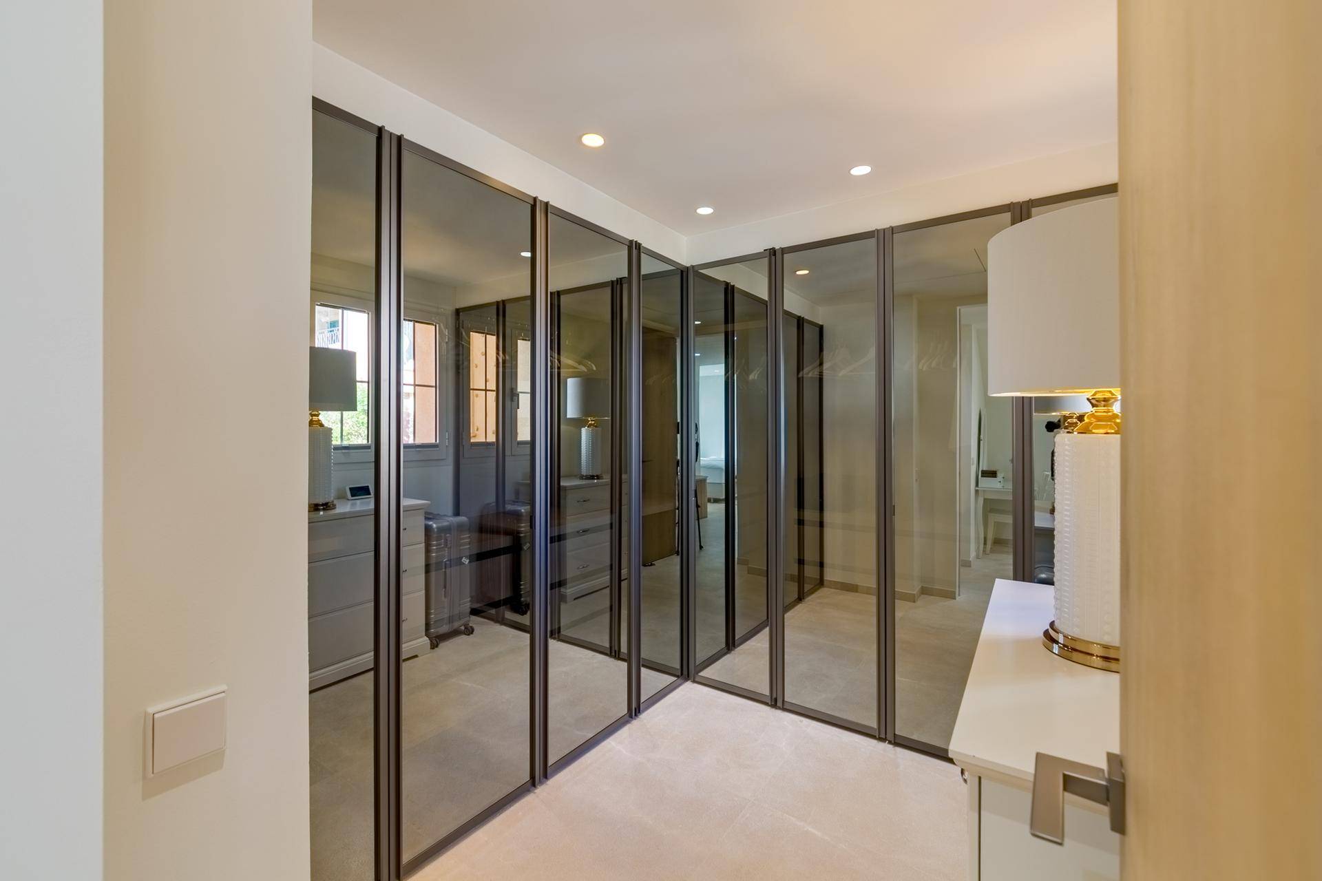 Luxuriöser begehbarer Kleiderschrank mit raumhohen Spiegeltüren und Teppichboden.