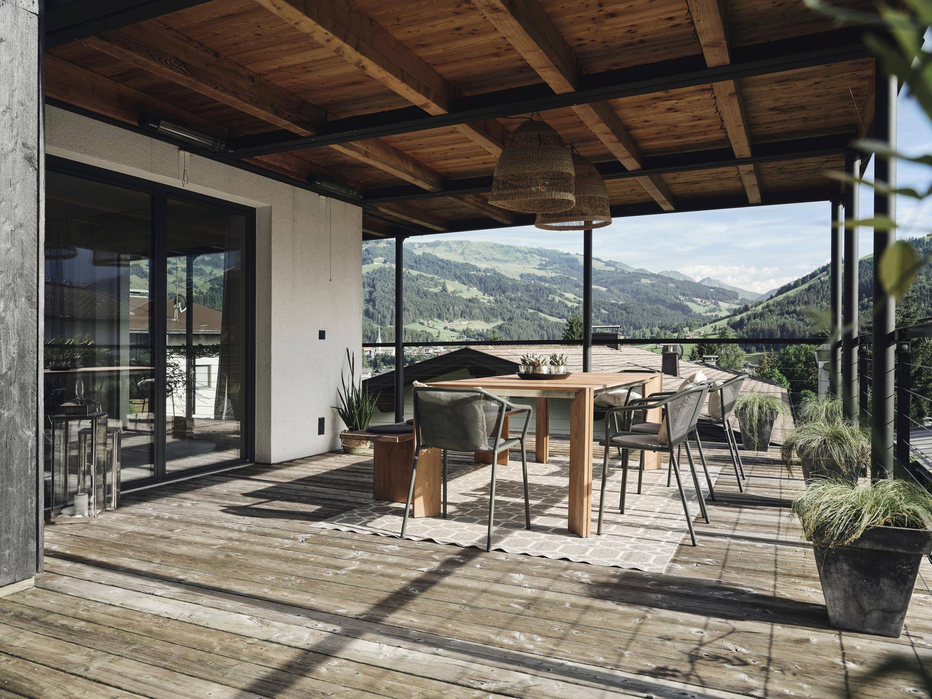 Überdachte Holzterrasse mit Esstisch und Stühlen, bietet einen weiten Blick auf die umliegende Berglandschaft.