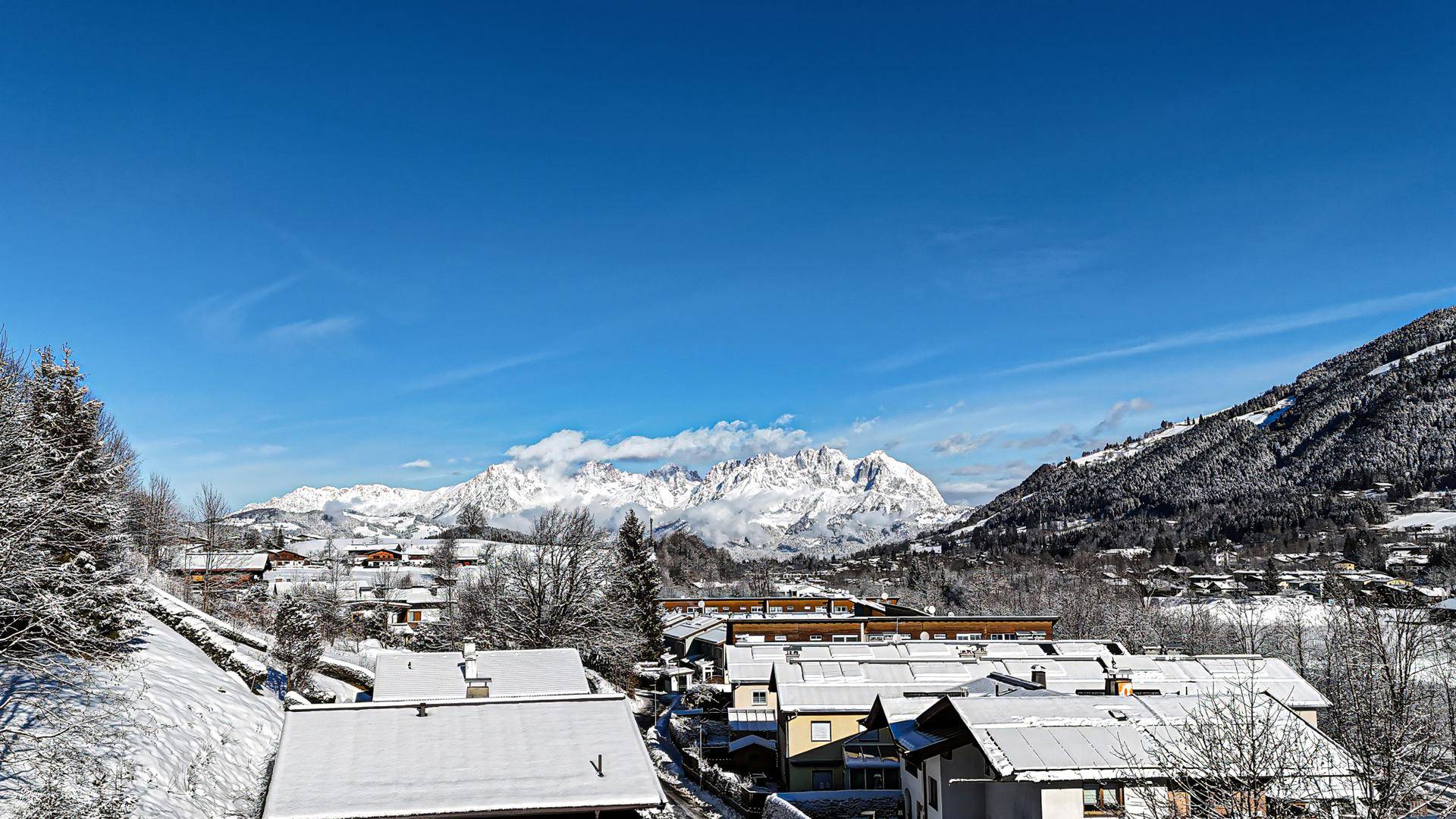 Weitläufiger Blick über ein schneebedecktes Dorf mit majestätischen Bergen im Hintergrund.