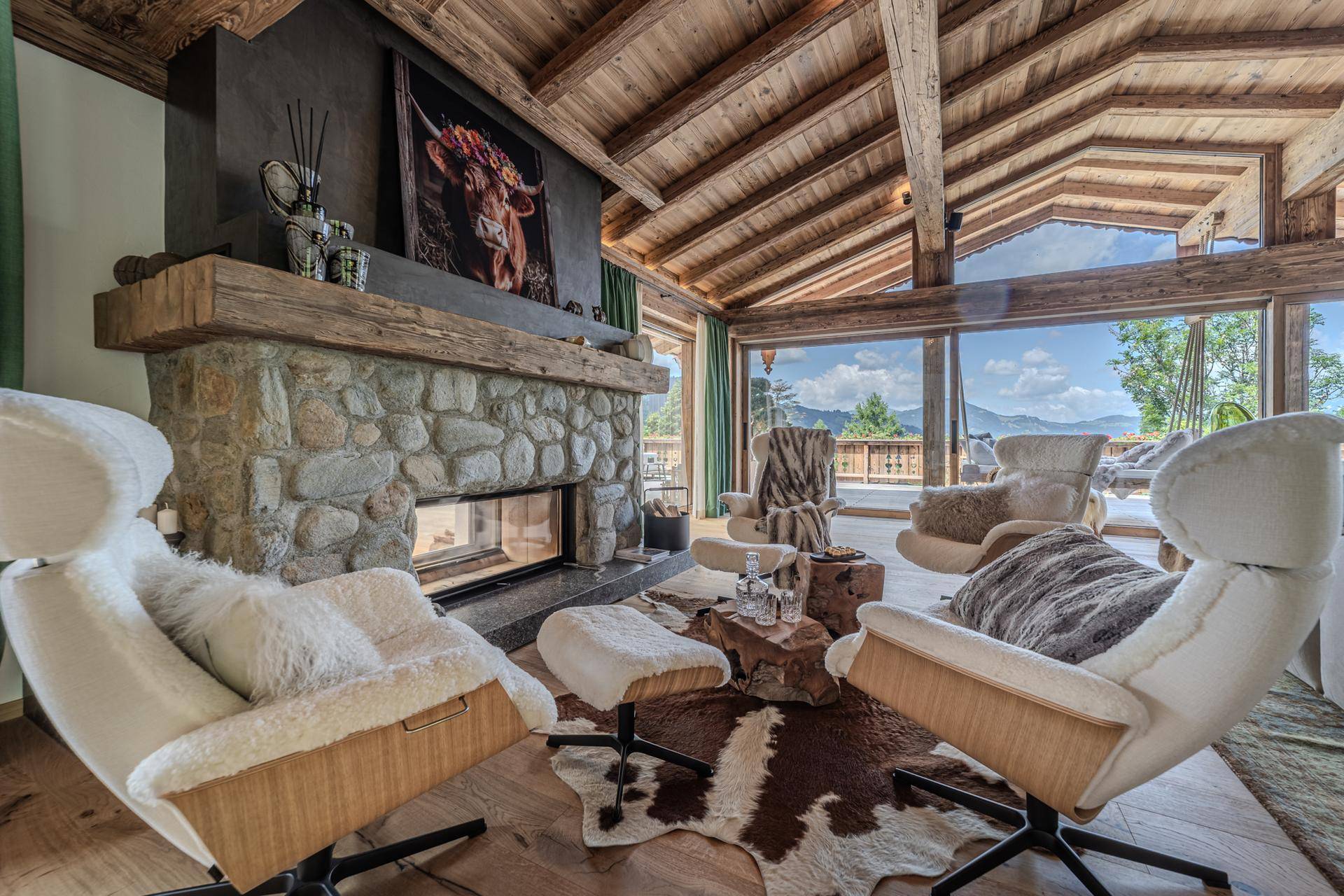 Gemütliche Sitzecke im Wohnzimmer mit Steinkamin, Fellteppich und Panoramablick auf die Berge.