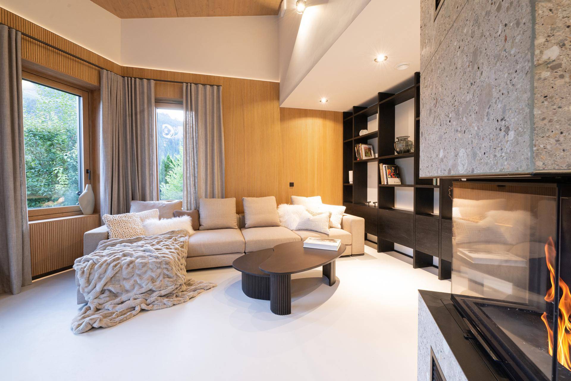 Gemütlicher Wohnbereich mit beigem Sofa, Holzwänden und integriertem Kamin, bietet Blick ins Grüne.