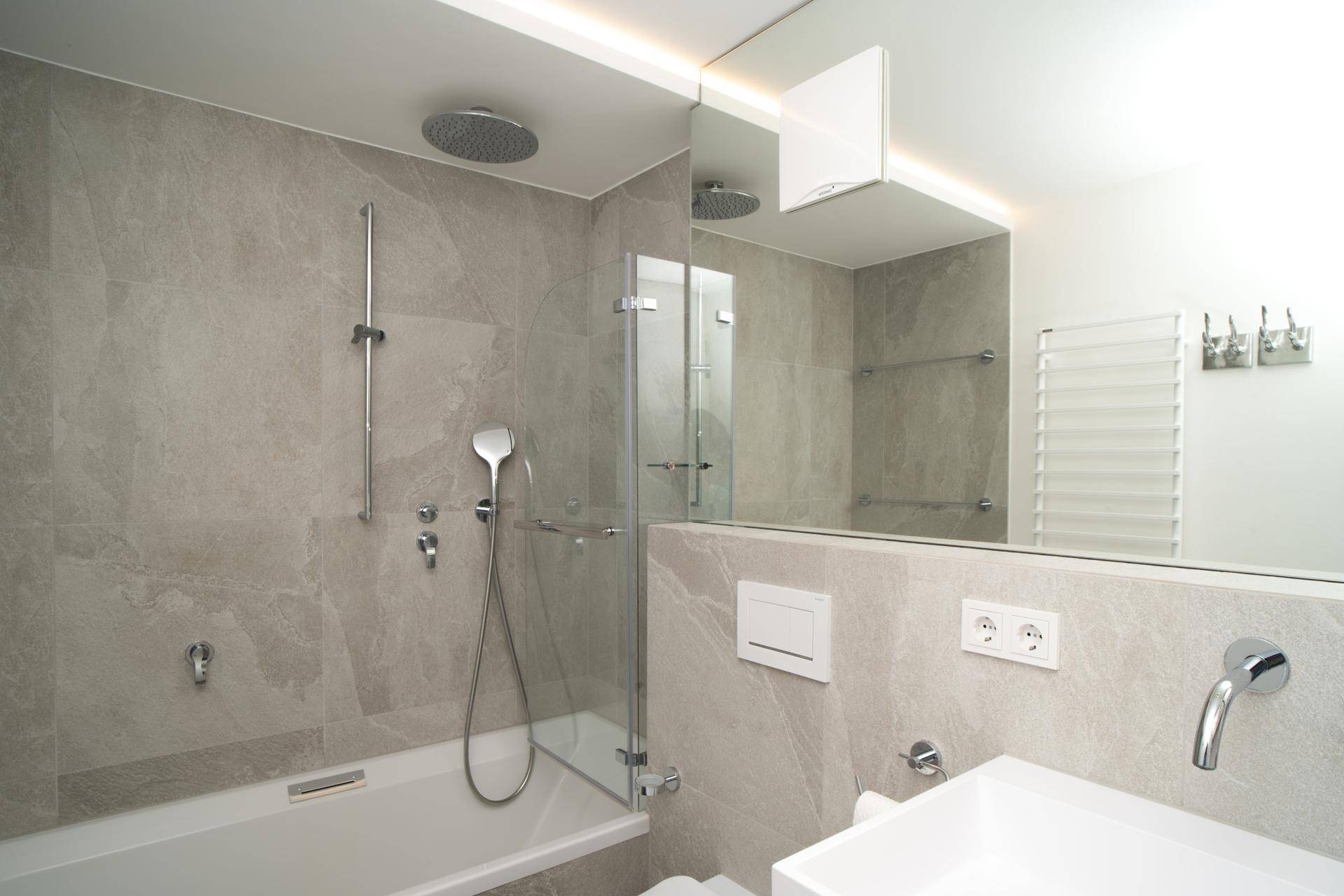 Modernes Badezimmer mit grauen Fliesen, Badewanne, Dusche und beheiztem Handtuchhalter.