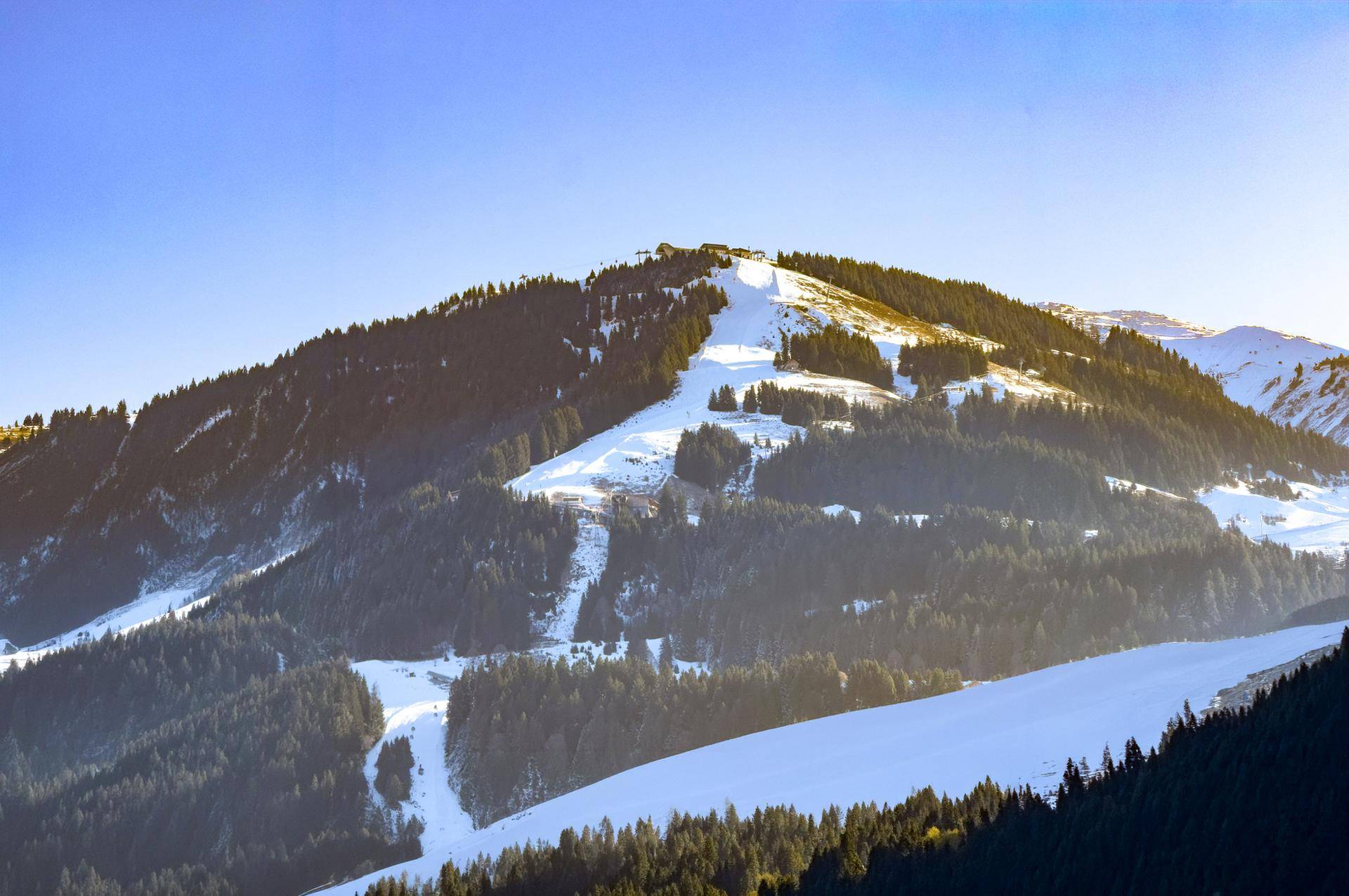 Panoramablick auf einen schneebedeckten Berg mit Skipisten und dichten Wäldern unter klarem Himmel.