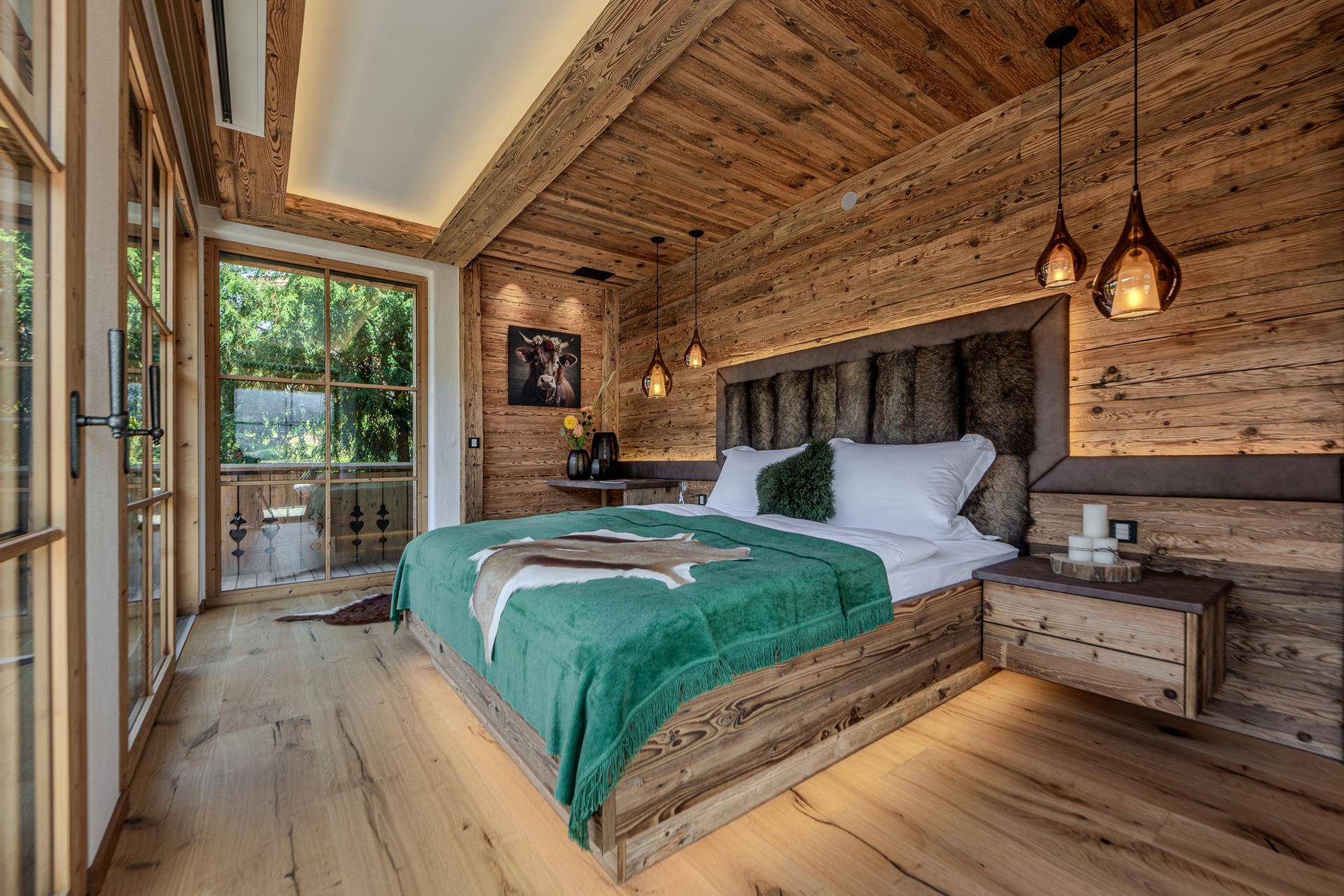 Gemütliches Schlafzimmer im alpinen Stil mit Holzwänden, Holzbalkendecke und Balkonzugang.