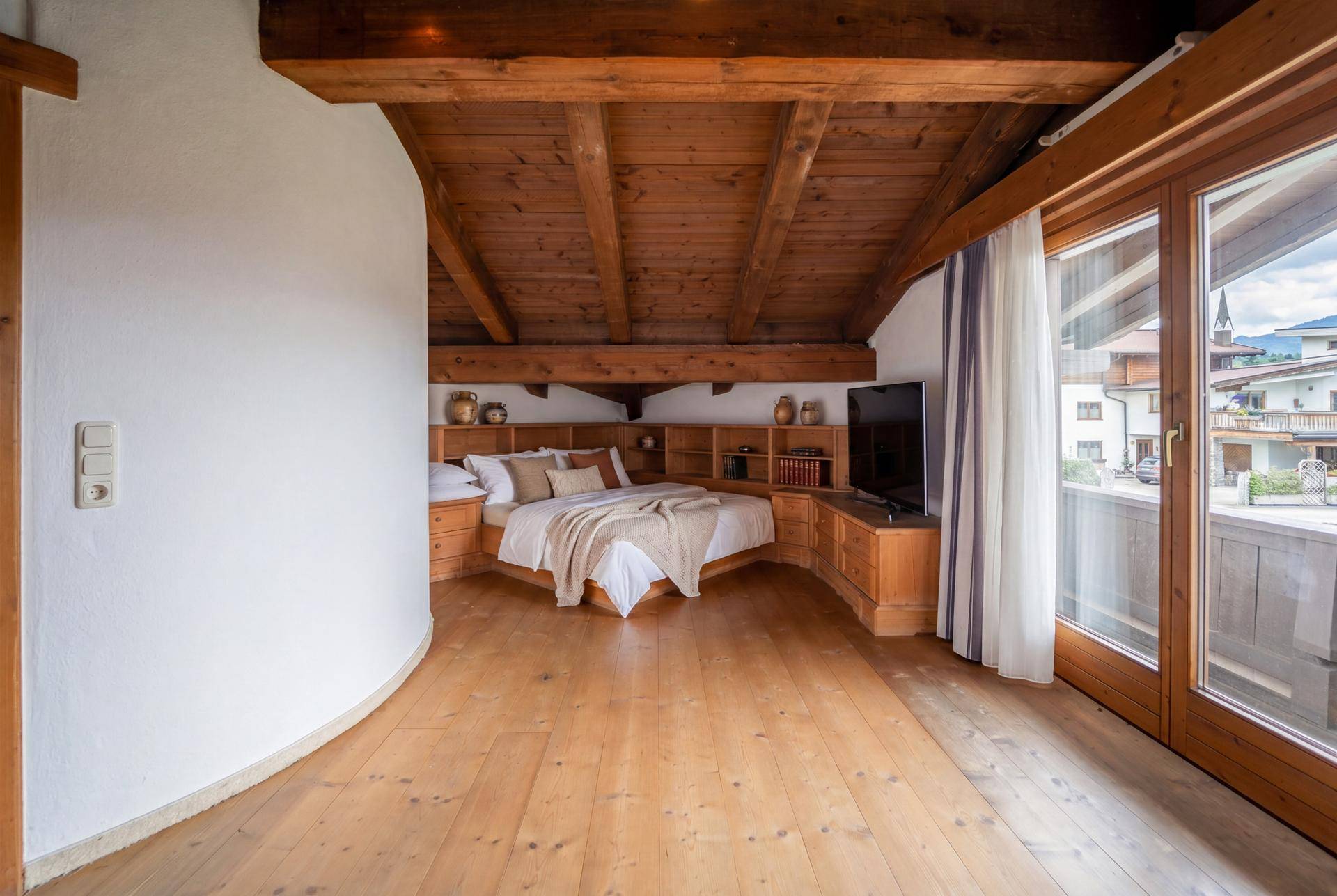 Schlafzimmer mit Holzbalkendecke, integriertem Bett und Zugang zu einem Balkon.