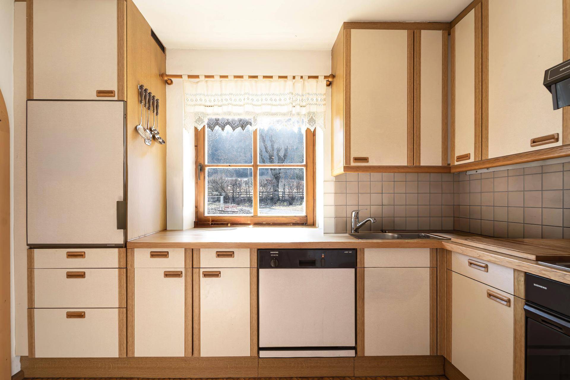 Funktionale Küche im Landhausstil mit Holzfronten, Spülmaschine und Fensterblick ins Grüne.