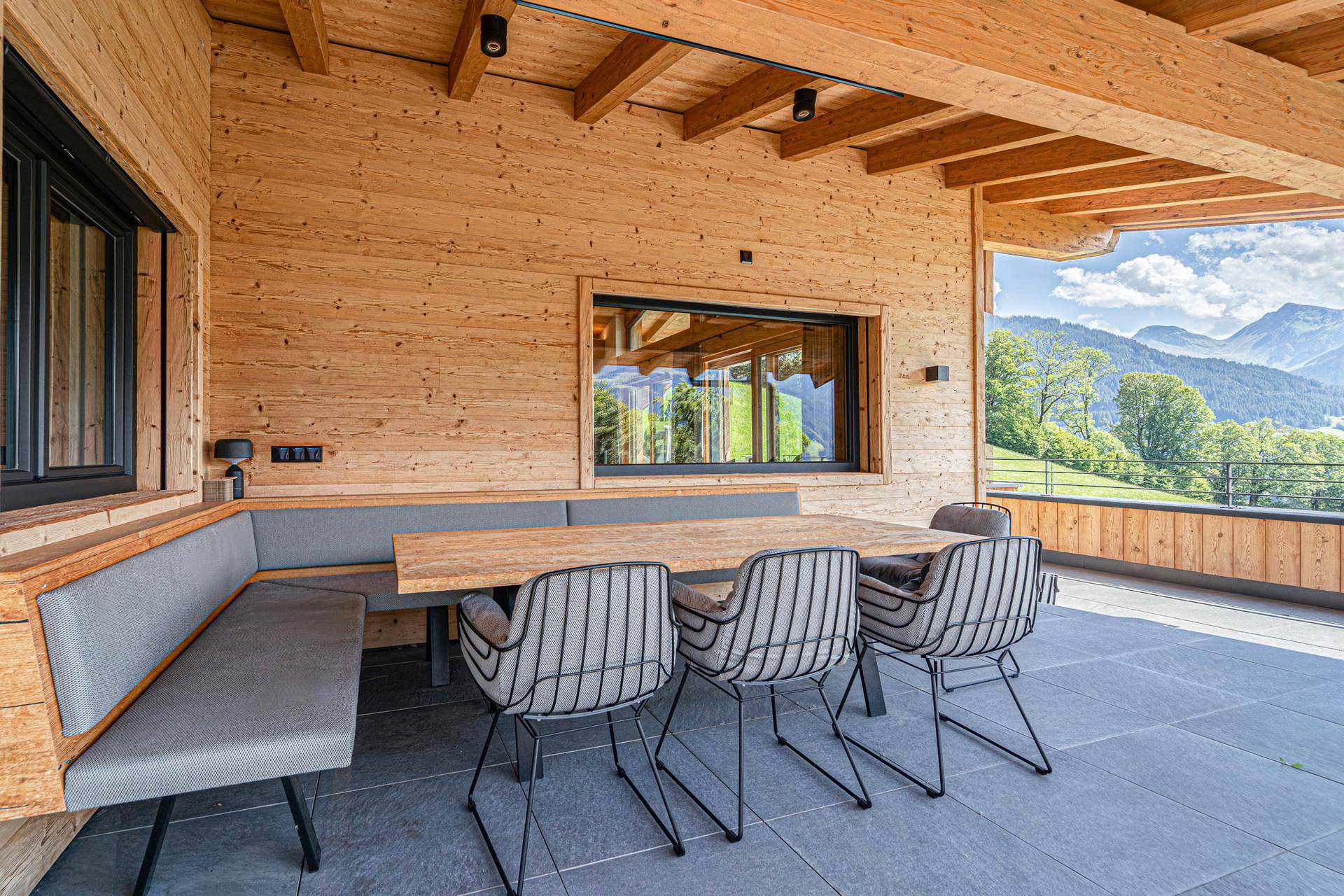 Gemütlicher überdachter Außenbereich mit Holzbänken, Esstisch und herrlichem Bergblick.