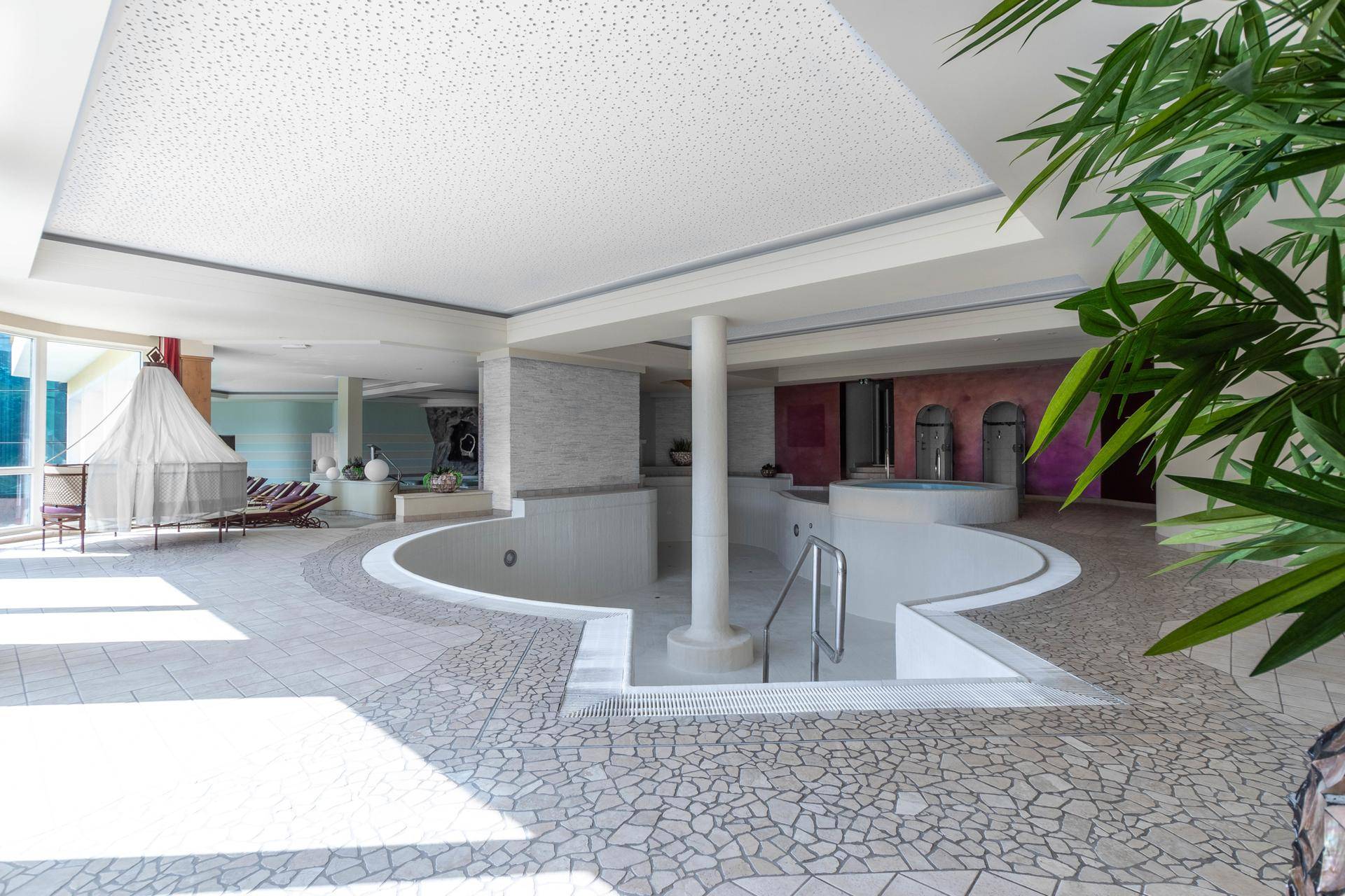 Geräumiger Wellnessbereich mit verschiedenen Becken, Liegeflächen und Pflanzen, ideal zur Entspannung.